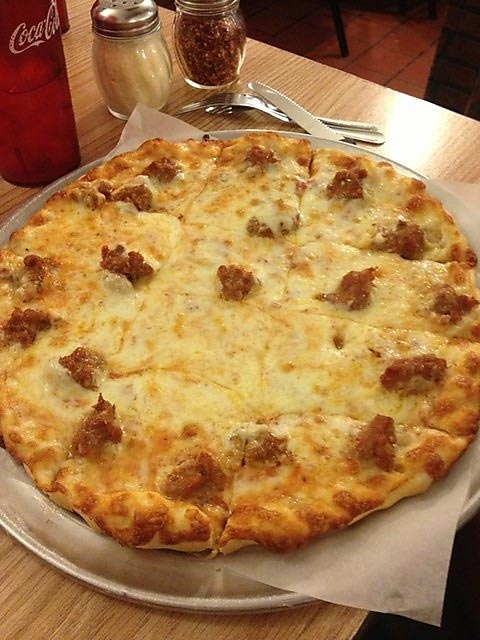 A sausage pizza on a metal pan at the table.