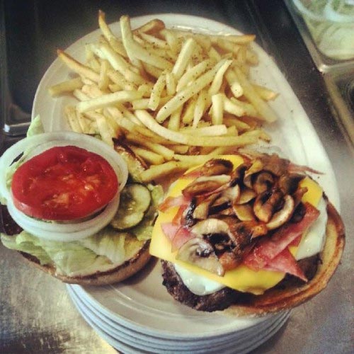 A mushroom and swiss burger with bacon, plated with fries.