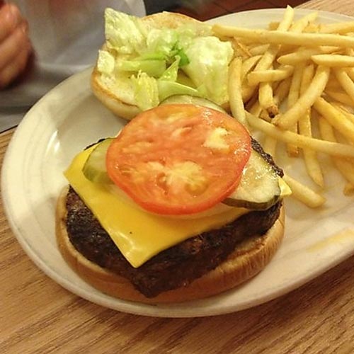 A cheeseburger with tomato and pickle, served with fries.