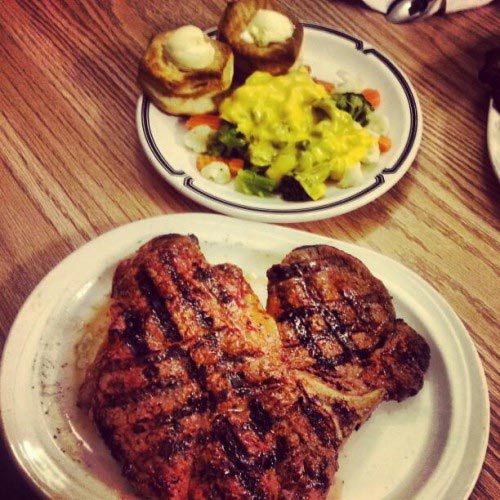 A grilled T-bone steak with baked potato and vegetables.